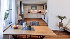 Una cucina moderna con mobili bianchi, un tavolo da pranzo in legno e un piccolo tavolino con una pianta.