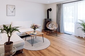 A modern living room with a sofa, a round coffee table, a potted plant, a wicker chair, and a wood-burning stove. - Vacation apartment 1 Sonnenblick on the first floor with 2 terraces and garden (Riedering)