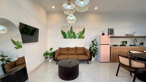 Een moderne woonkamer met een bank, een salontafel en een eethoek met stoelen. Er is een keuken met een koelkast en een spoelbak.