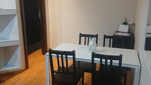 Ein Essbereich mit einem weißen Tisch, vier Holzstühlen, einem weißen Schrank und einer kleinen Regaleinheit.