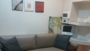 Ein Wohnzimmer mit grauem Sofa, Holzboden und einer weißen Wand mit drei Kunstwerken.