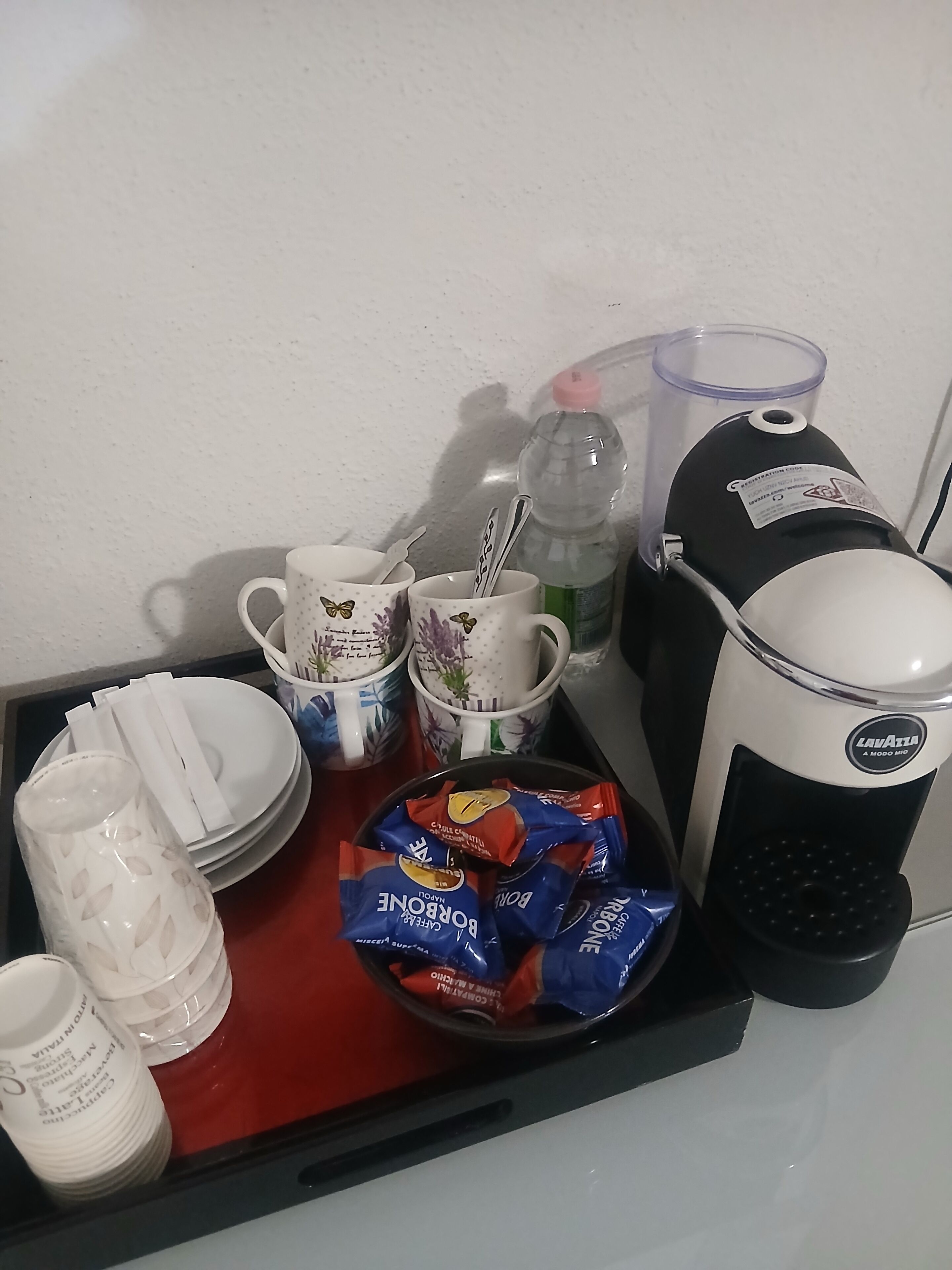 A kitchen counter with a coffee maker, a water bottle, and various kitchen items like cups, plates, and napkins.