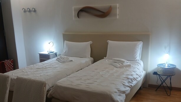 Ein Hotelzimmer mit zwei Betten, einem kleinen Tisch und einem Stuhl. Nachttische mit Lampen sowie eine Wandleuchte sind vorhanden.