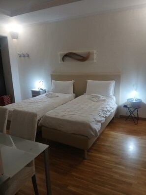 A hotel room with two beds, a small table, and a chair. There are bedside tables with lamps and a wall-mounted light fixture. - Stefano House Fontana di Trevi (Rome)