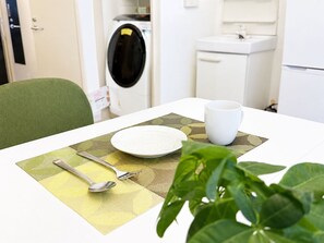 A dining table with a plate, a cup, and cutlery set on a placemat, with a green chair and a plant in the foreground. - Near Shinjuku , Shibuya Area , 6 Guests , Family Stay (渋谷区)