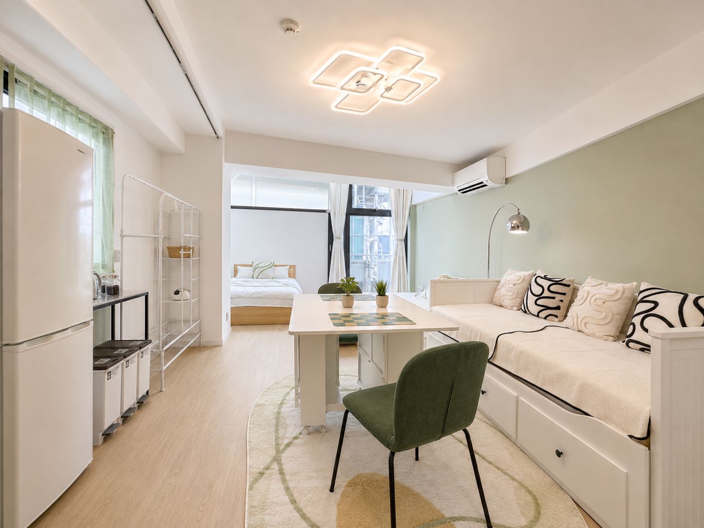 A compact hotel room with a bed, a desk, a chair, a sofa, and a kitchenette.