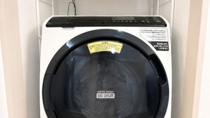 Una lavadora de carga frontal con panel de control, ubicada en un cuarto de lavado con estantes arriba.