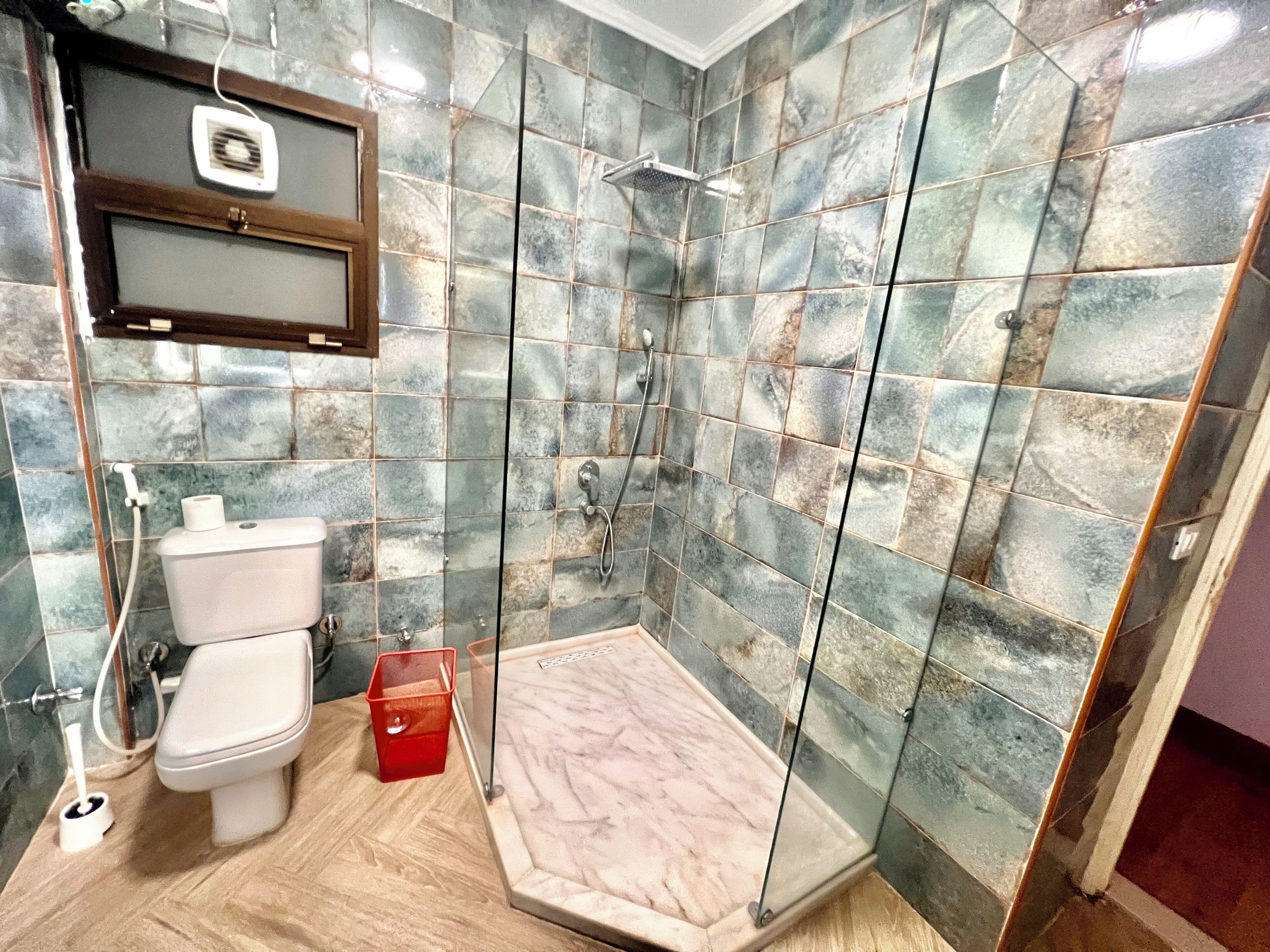 Un baño con ducha, inodoro y un cubo de basura rojo.
