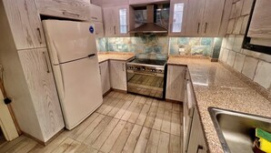 Una cocina con armarios de madera, un lavamanos de acero inoxidable, una estufa y un refrigerador.