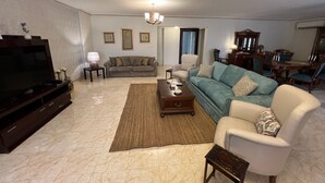 Una sala de estar con televisor, sofá, sillón, mesa de centro y comedor.