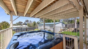 Een hottub onder een houten pergola met uitzicht op een achtertuin en omliggende huizen.