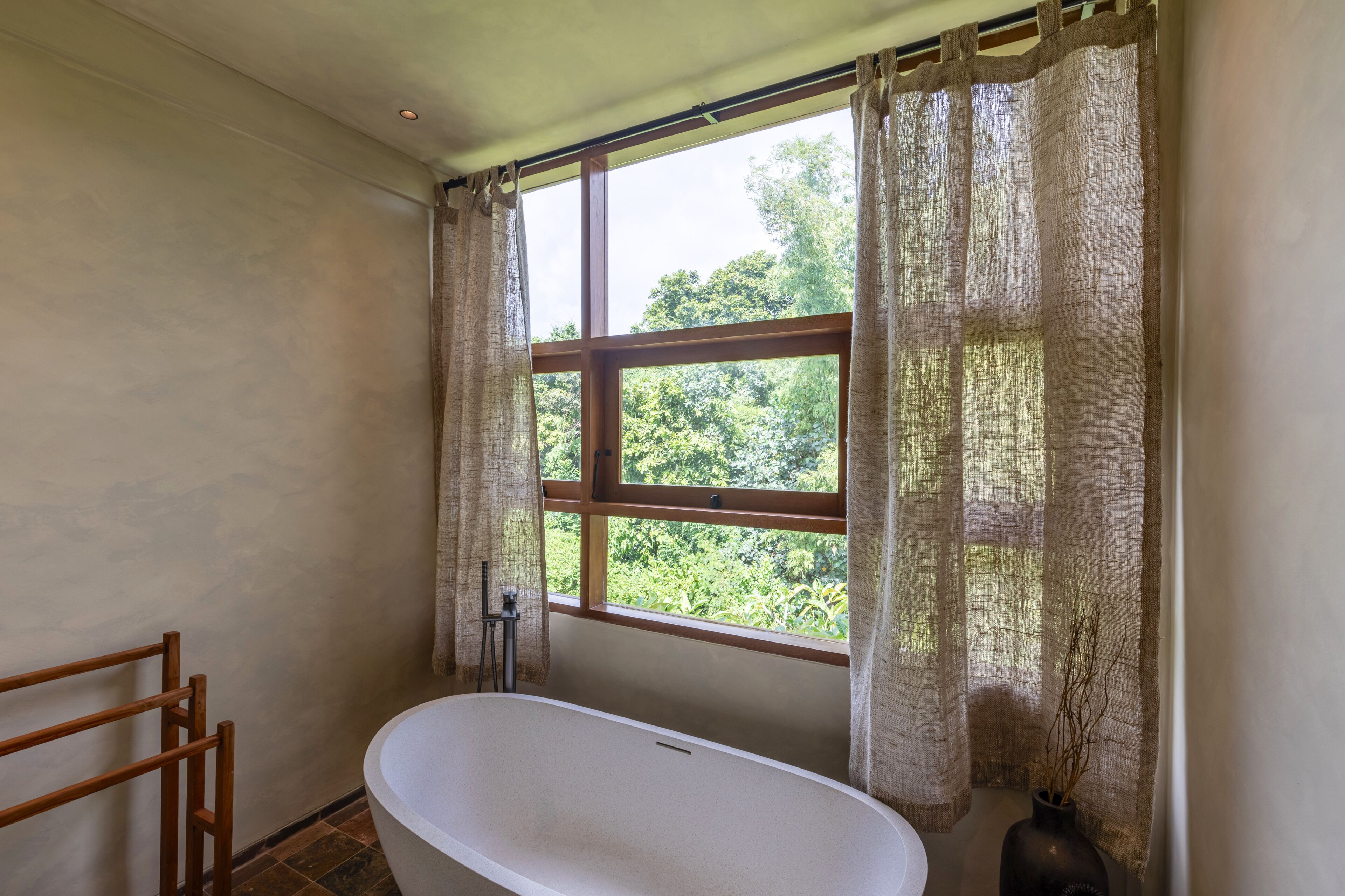 Un baño con bañera, una ventana con cortinas y vistas al exterior.