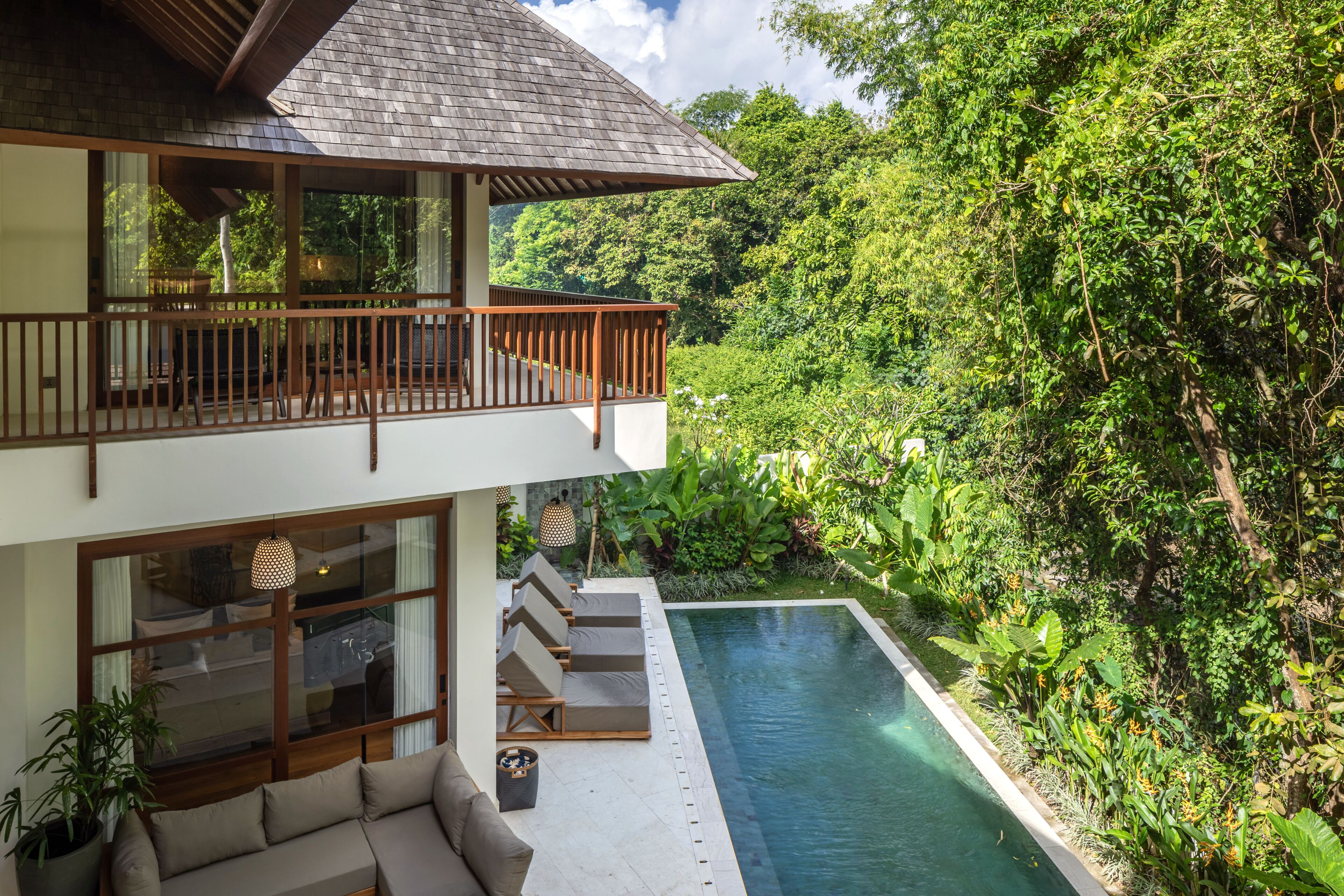 A two-story building with a balcony, a pool, and lush greenery.