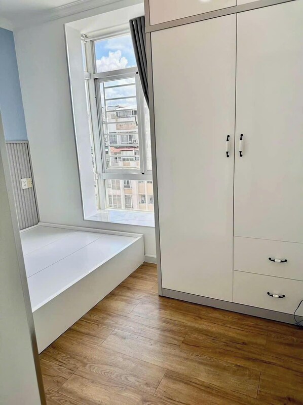 A room with a built-in bench under a window, a wardrobe with multiple doors, and wooden flooring. - Sky Garden 3 Apartment by Diamond Suite (Ho Chi Minh City)