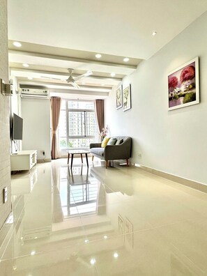 A spacious living room with a glossy floor, a grey sofa with cushions, a flat-screen TV, and a dining area with a table and chairs. - Sky Garden 3 Apartment by Diamond Suite (Ho Chi Minh City)