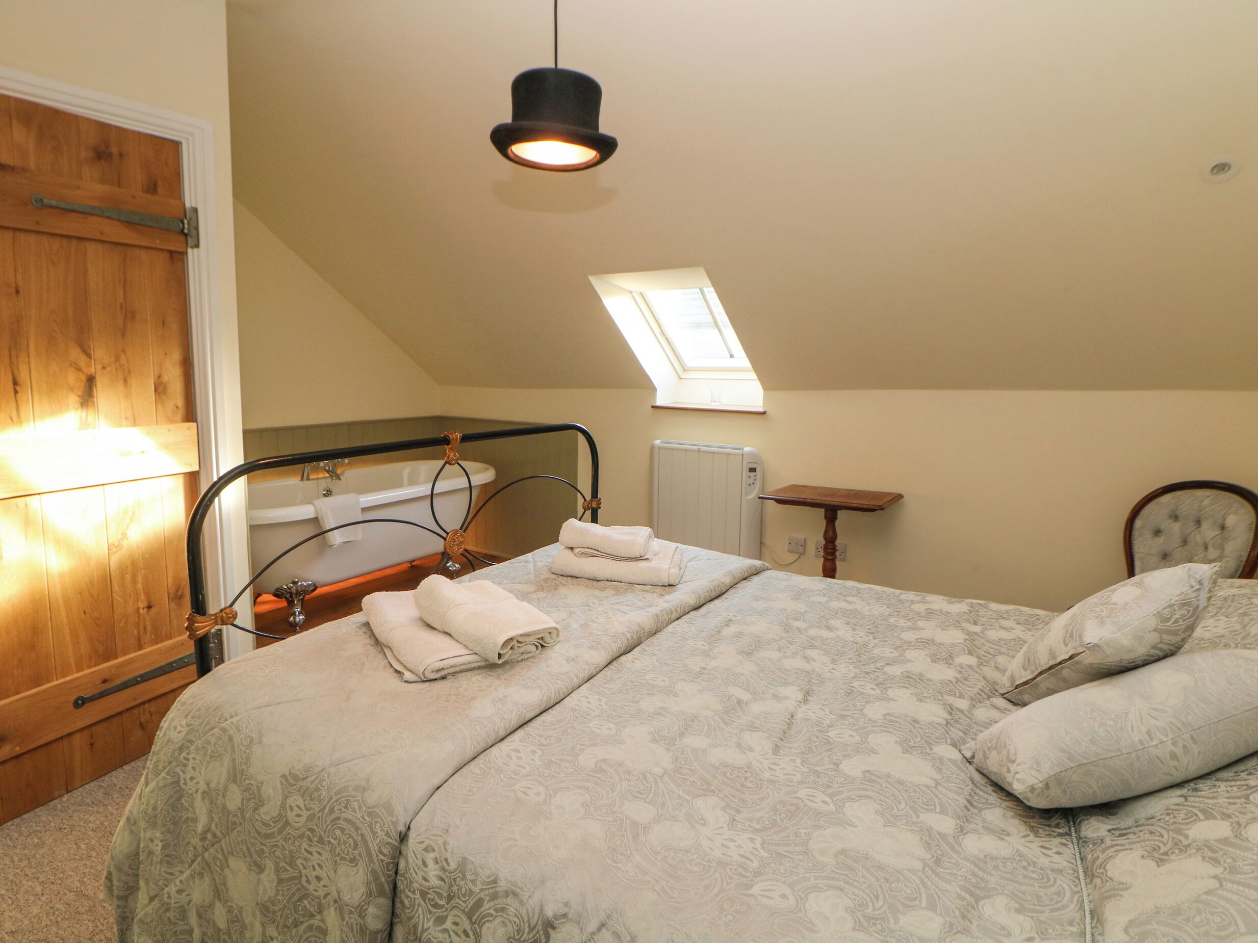 Ein Schlafzimmer mit Bett, Holztür, Heizkörper, einem kleinen Tisch und einem Fenster.