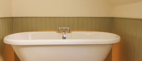 A freestanding bathtub with claw feet in a corner of a room with wooden flooring and a green wall.