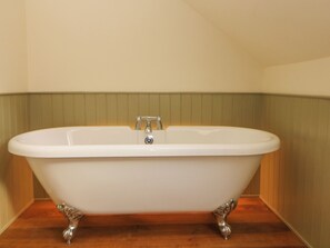 A freestanding bathtub with claw feet in a corner of a room with wooden flooring and a green wall. - Laneside Barn (Hope Valley)