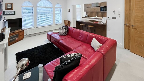 Een moderne woonkamer met een rode leren bank, een televisie en een keuken met een barkruk.