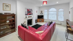 A living room with a red sofa, a fireplace, a television, and a dining area with a table and chairs. - Modern coastal escape, 2 minutes from the beach, cafés and bars. (St. Leonards-on-Sea)