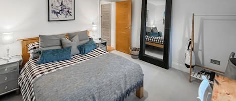 A bedroom with a bed, bedside table, lamp, and a mirror.