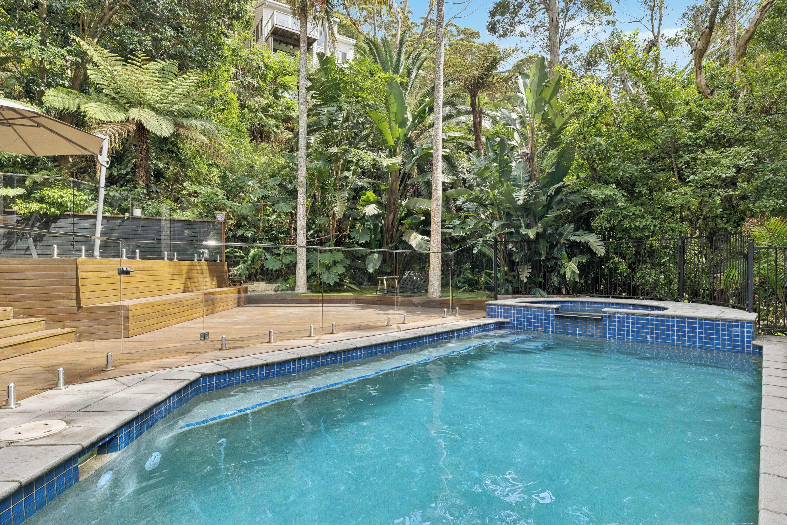 Una piscina con borde de azulejos, rodeada de exuberante vegetación y una terraza de madera.