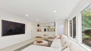 A modern living room with a large painting, a sofa, a coffee table, and a kitchen area in the background. - Pool & Spa Oasis. Home Theatre. Sleeps 8 (North Avoca)