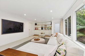 Ein modernes Wohnzimmer mit einem großen Gemälde, einer Couch, einem Couchtisch und einer Küchenzeile im Hintergrund.