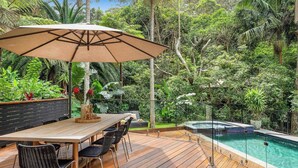 An outdoor deck with a wooden table and chairs, a large umbrella, and a swimming pool. - Pool & Spa Oasis. Home Theatre. Sleeps 8 (North Avoca)