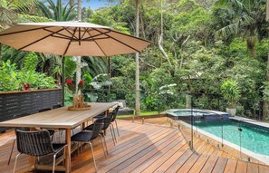 Eine Terrasse im Freien mit Holztisch und -stühlen, einem großen Sonnenschirm und einem Swimmingpool.