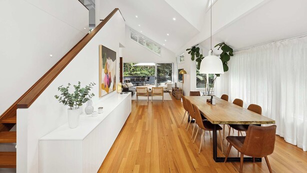 A spacious dining area with a long wooden table and multiple chairs, a staircase with a wooden railing, and a large window providing natural light. - Pool & Spa Oasis. Home Theatre. Sleeps 8 (North Avoca)