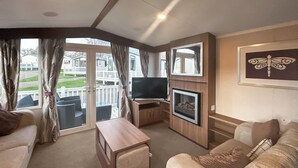 Una sala de estar con sofá, televisión, chimenea y balcón con cortinas.
