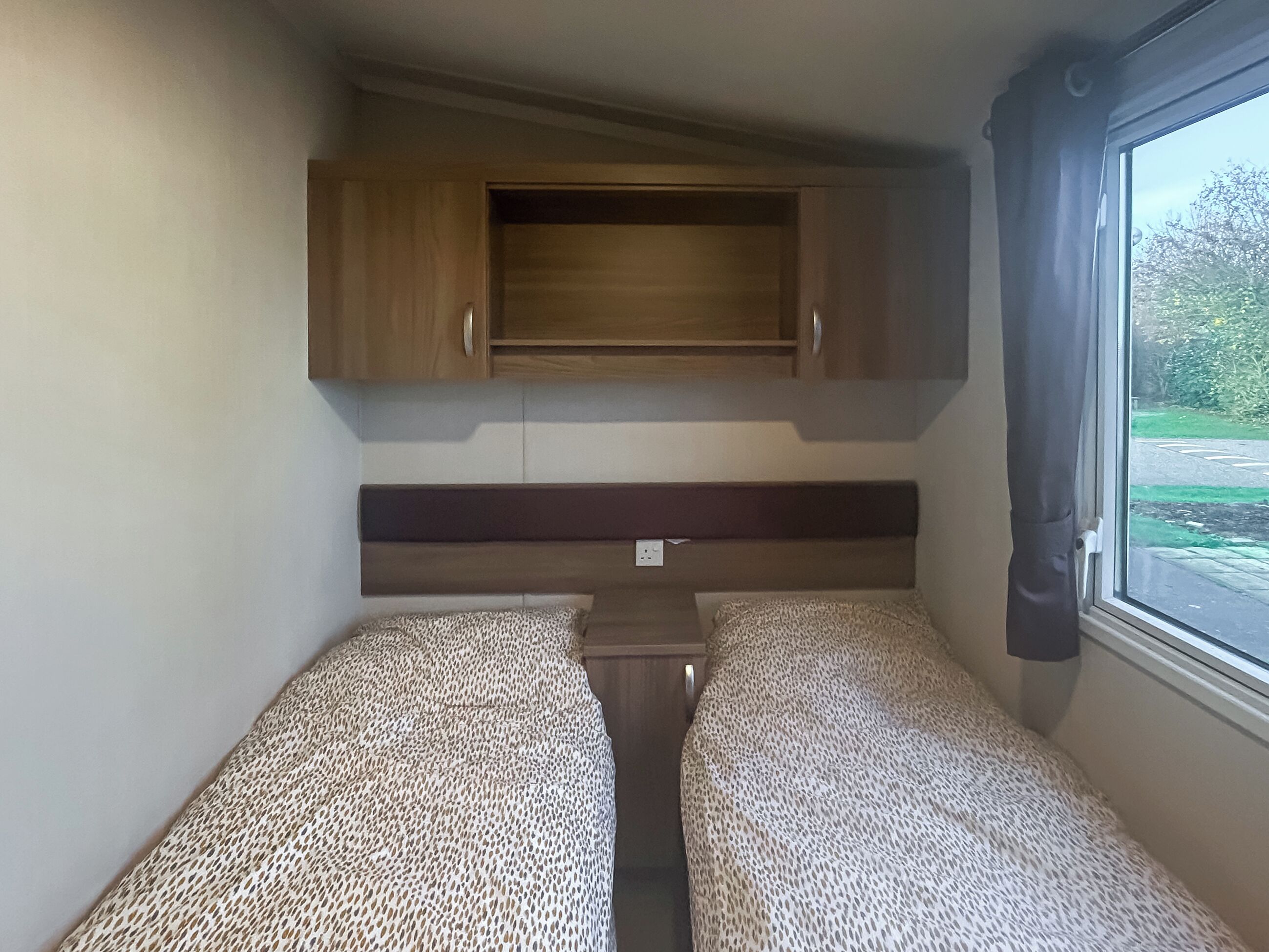 A compact RV interior with two beds, a central table, and a window with curtains.