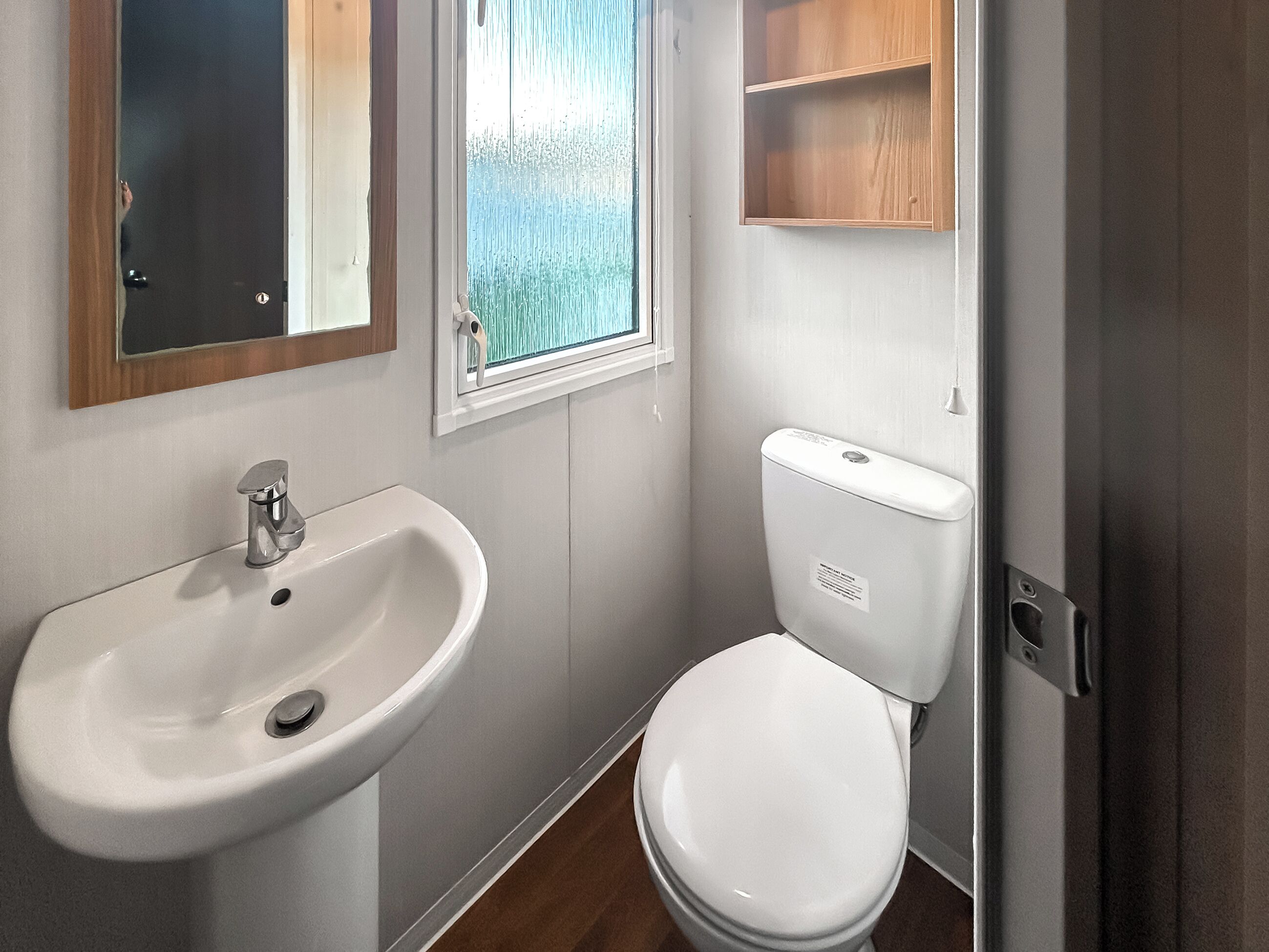 A bathroom with a white sink, toilet, and a window with a view of trees.