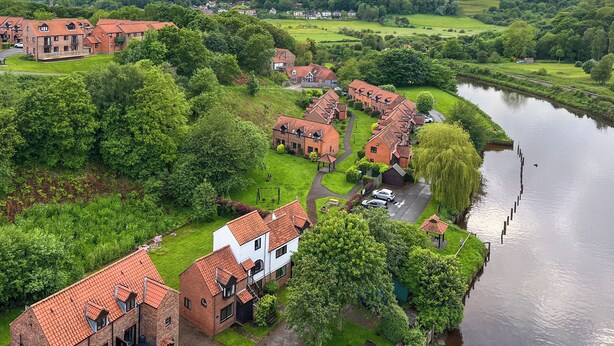 Un quartier résidentiel situé au bord de la rivière, avec des maisons en briques, de jolies pelouses verdoyantes et un ciel dégagé.