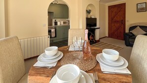 Une table à manger dressée avec de l’assiette, des bols et des couverts blancs, et une bouteille de champagne placée au centre.