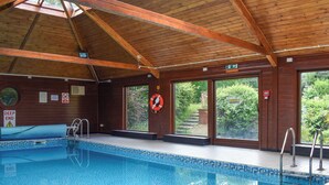 Une piscine intérieure avec des poutres en bois, une bouée de sauvetage et un panneau indiquant « Zone profonde ».