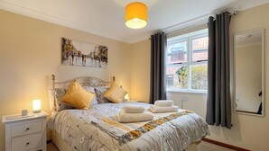 Une chambre bien rangée, avec un lit, une table de chevet, une lampe et une fenêtre avec des rideaux.