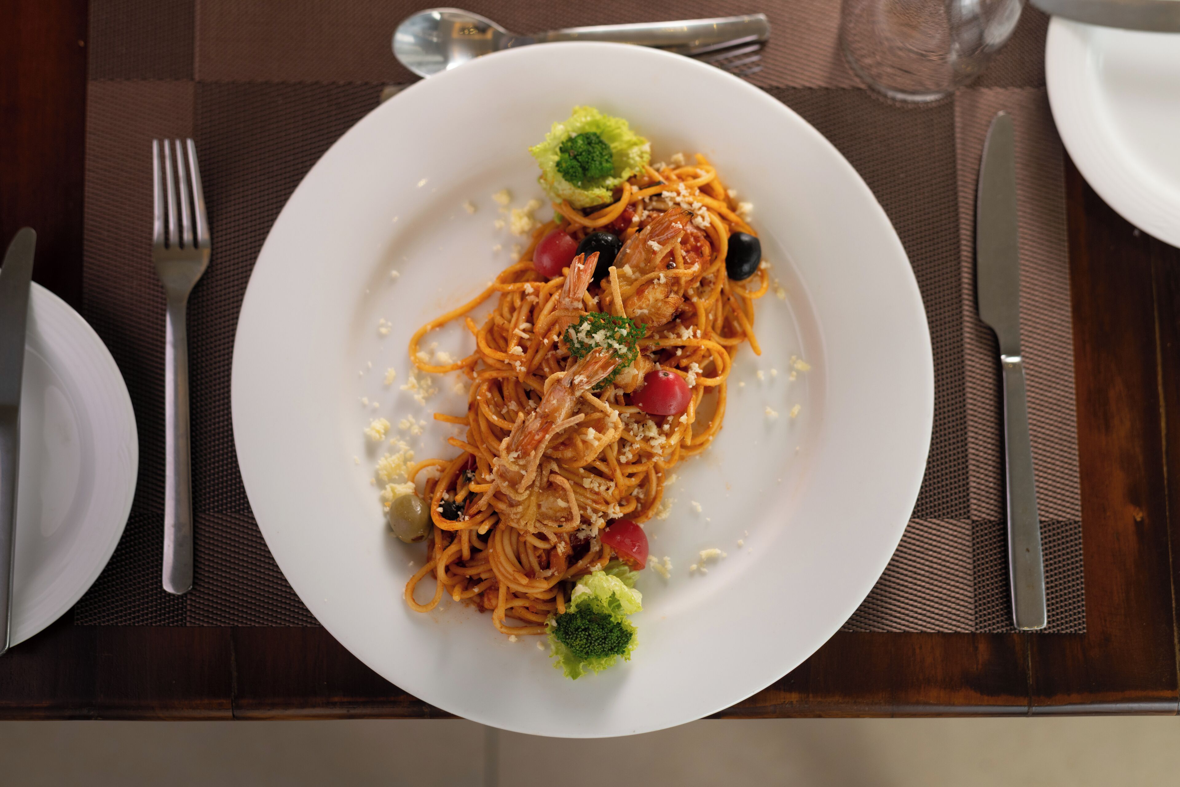Un plato de espagueti con camarones, tomates cherry y brócoli sobre un plato blanco.