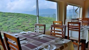 Comedor con una mesa dispuesta para cuatro personas, amplias ventanas con vistas a colinas verdes.
