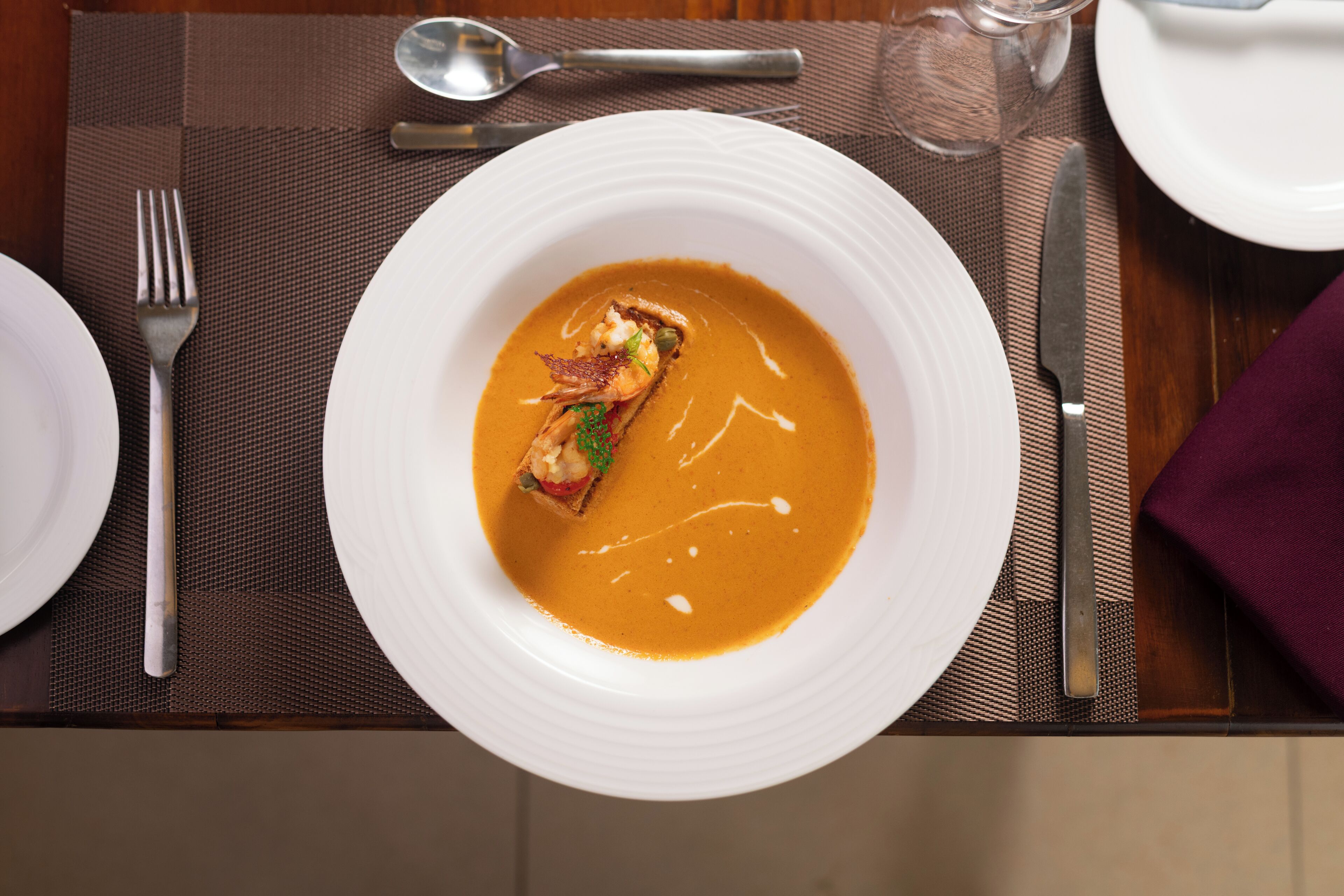 A dining table with a white plate containing a soup dish, a fork, a knife, and a spoon.