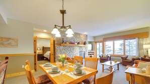 A dining area with a wooden table set for four, surrounded by chairs with floral upholstery. A stone wall and a fireplace are visible in the background. - Pool Access: North Shore Gem Near Beaches & Trails (Two Harbors)
