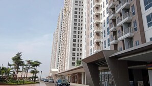 A high-rise residential building with multiple balconies, a covered entrance, and a parking area with cars. - Apartemen Tokyo Riverside by Linkara (Teluknaga)