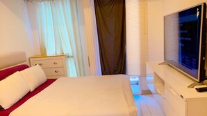 A hotel room with a bed, a TV, a desk, and a window with curtains. - Apartemen Tokyo Riverside by Linkara (Teluknaga)