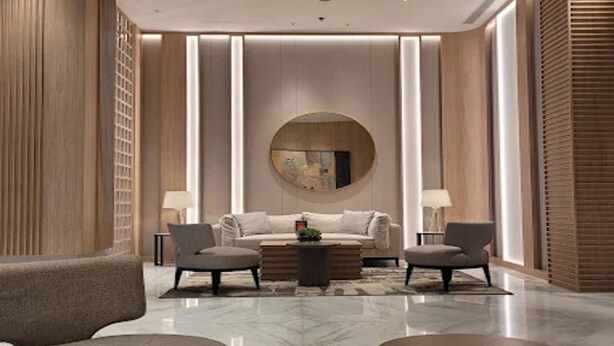 A modern living room with a sofa, two armchairs, a coffee table, and a round mirror on the wall. - Apartemen Tokyo Riverside by Linkara (Teluknaga)