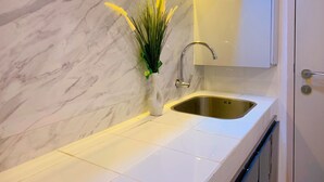 A kitchen with a marble backsplash, a stainless steel sink, and a white cabinet. - Apartemen Tokyo Riverside by Linkara (Teluknaga)