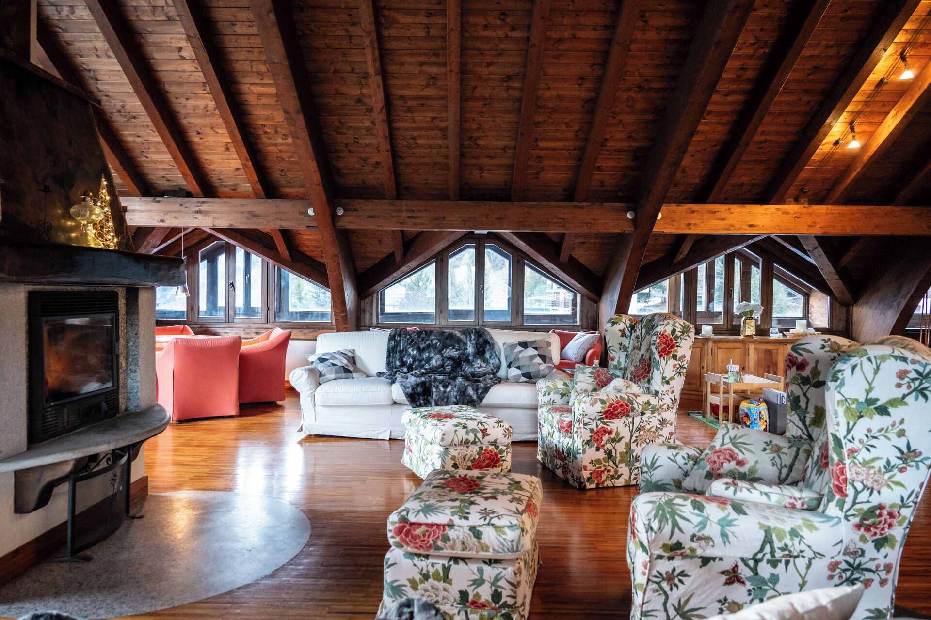 Un acogedor espacio tipo loft con techo de madera, chimenea y un gran ventanal con vistas a un bosque.