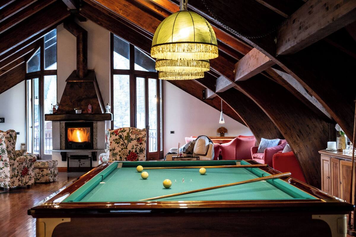 A cozy room with a pool table, floral armchairs, and a large window.