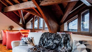 A cozy attic room with wooden beams, a white sofa, and a red chair. - Rifugio Genzianella (Varzo)