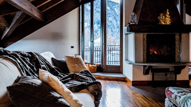 A cozy living room with a wooden ceiling, a fireplace, and a view of a snowy mountain. - Rifugio Genzianella (Varzo)